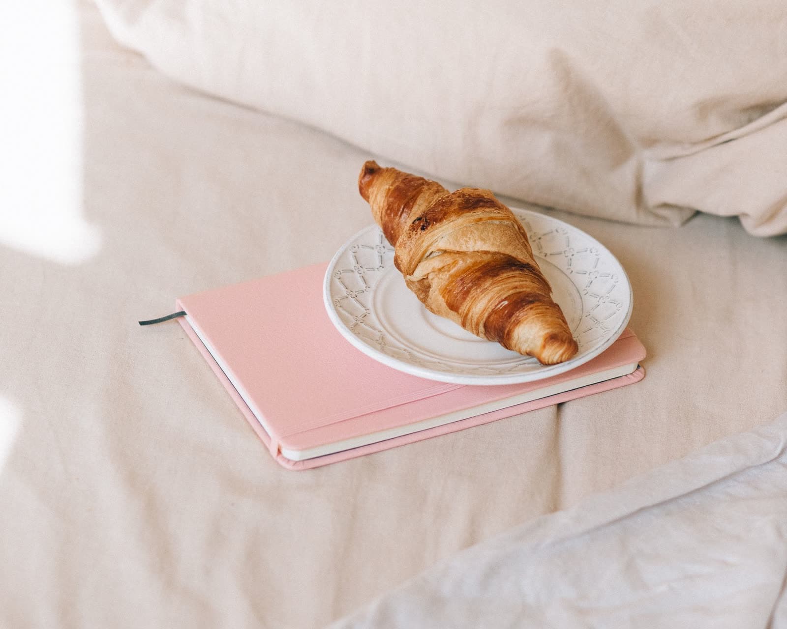 Un croissant posé sur un carnet rose, au petit matin